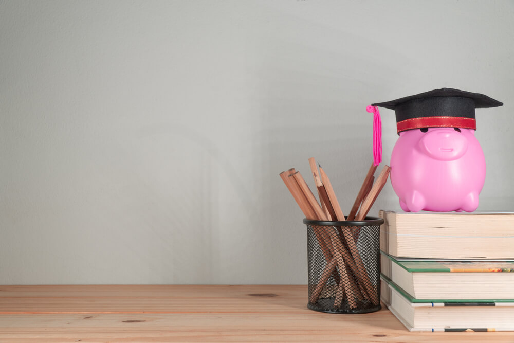 a pink piggy bank wearing a graduation cap on top of a pile of books