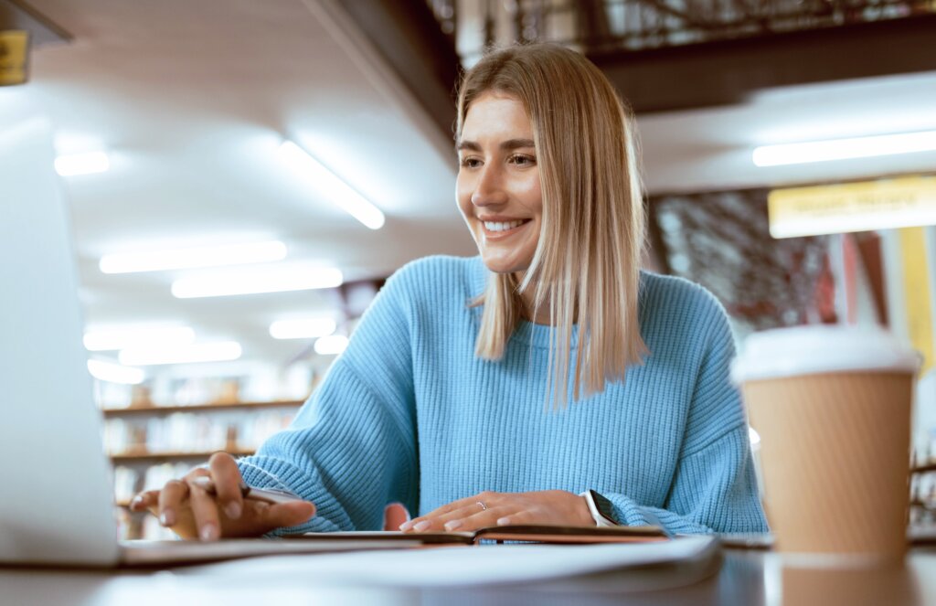 Blonde woman wearing a blue jumper drinking a coffee while deciding to study a PhD in London